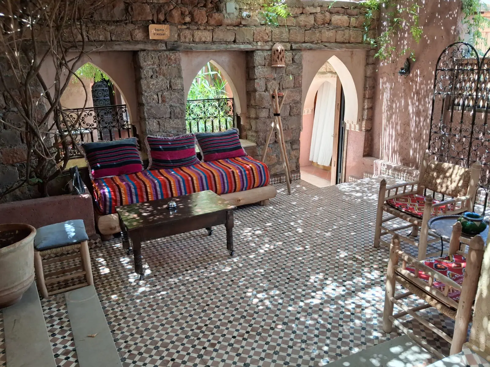 The welcome courtyard at Chambre d’hôtes Aya: stone arches, a zellige tiled floor and a striped Berber banquette under dappled light
