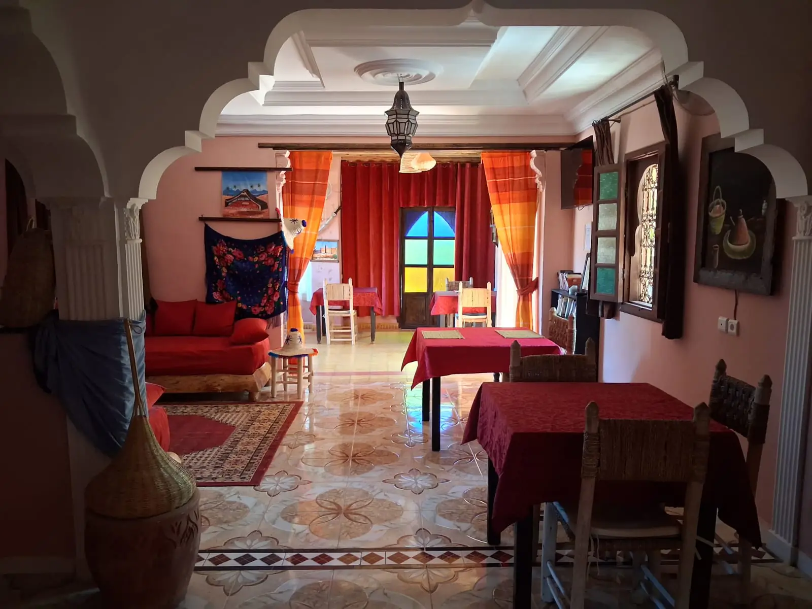 The salon at Chambre d’hôtes Aya where breakfast and dinner are served, with Moroccan arches, stained glass and red-clothed tables