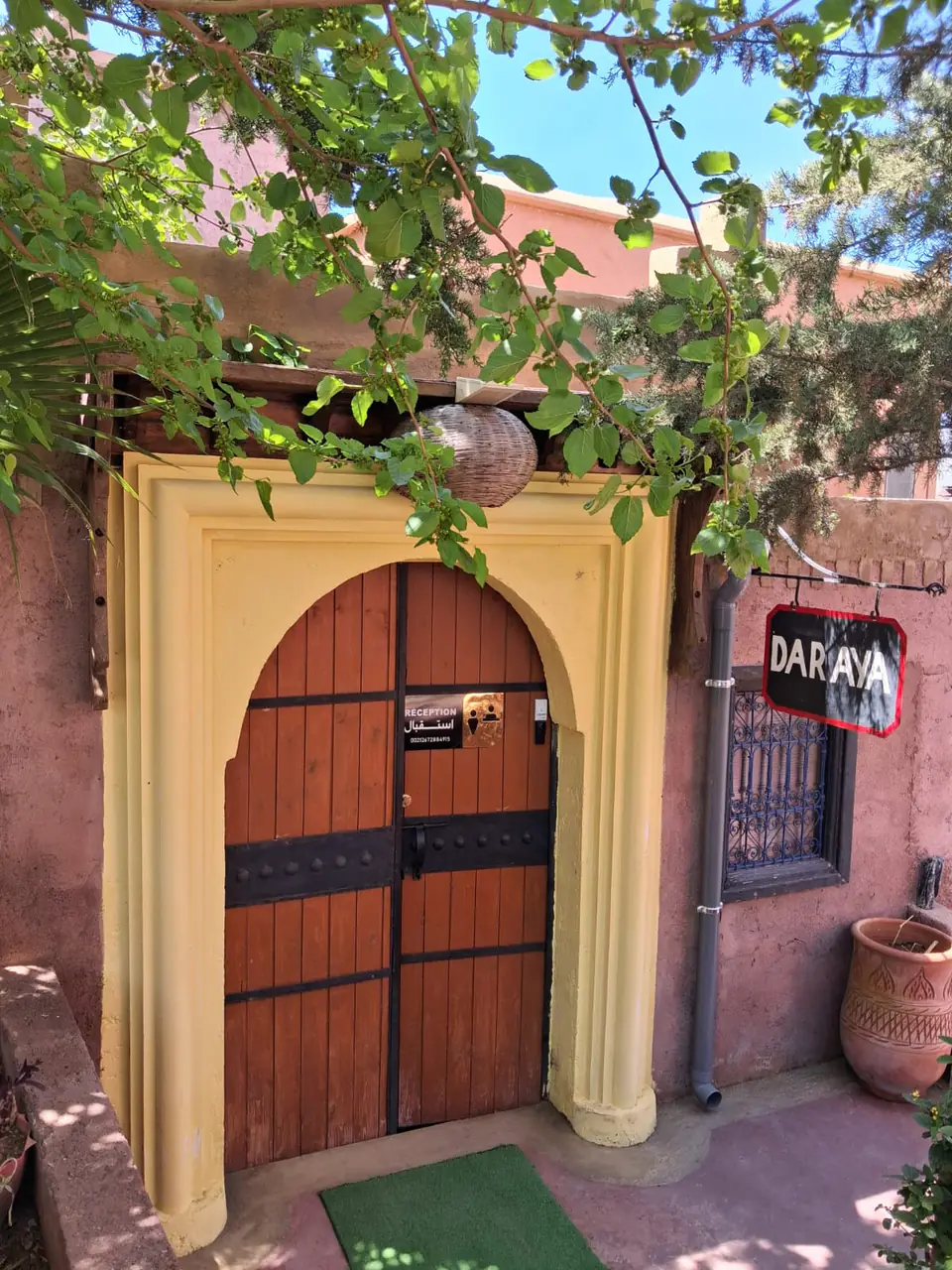 The carved wooden entrance door of Chambre d’hôtes Aya in Ouzoud, under its yellow arch beside the hanging “Dar Aya” sign