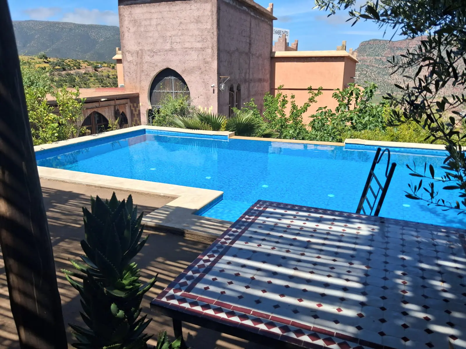 The outdoor pool at Chambre d’hôtes Aya in Ouzoud, with the earth-walled riad behind it and the Ouzoud gorge and Atlas foothills beyond