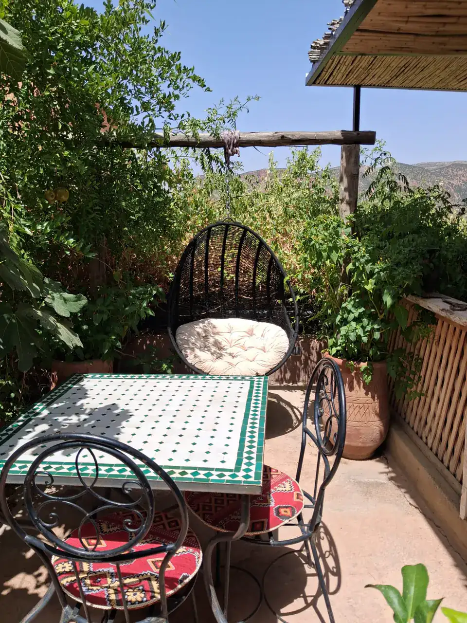 A hanging chair and a mosaic tile table on the terrace at Chambre d’hôtes Aya, looking towards the valley